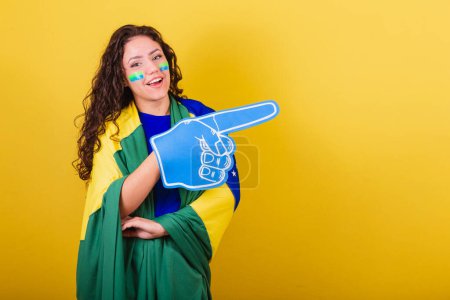 Foto de Mujer fanática del fútbol, fan de Brasil, copa del mundo, con guante de espuma. apuntando al espacio negativo, anuncio, texto o publicidad. Lado derecho. - Imagen libre de derechos