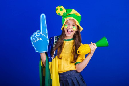 Téléchargez les photos : Jeune fille, fan de football du Brésil. habillé en chapeau et drapeau. utilisant doigt de mousse - en image libre de droit