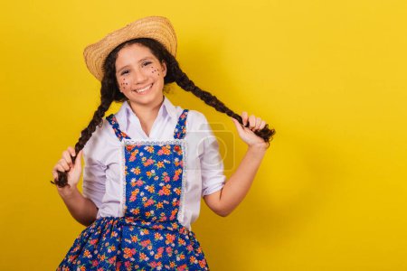 Foto de Chica vestida con ropa típica para Festa Junina. sosteniendo trenzas para el cabello y sonriendo. Para el Festival do Arraia - Imagen libre de derechos