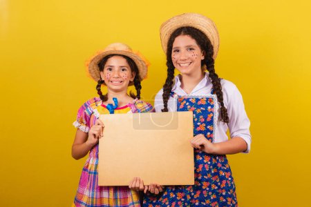 Photo for Sisters and friends, wearing typical clothes of the Festa Junina. Holding sign for text or advertisement. - Royalty Free Image