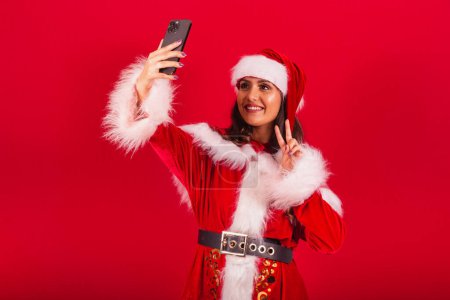 Foto de Mujer brasileña vestida con ropa de Navidad, Santa Claus. tomar foto autorretrato con smartphone. - Imagen libre de derechos
