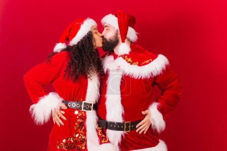 Téléchargez les photos : Couple brésilien, habillé pour Noël, Santa Claude, maman Claude. femme noire et homme caucasien. baiser. - en image libre de droit