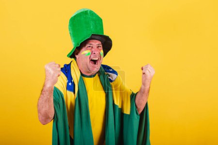 Foto de Hombre adulto, fanático del fútbol brasileño, con bandera y sombrero, celebrando. - Imagen libre de derechos