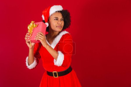 Foto de Hermosa mujer brasileña negra, vestida de santa claus, mamá claus, averiguar lo que es un regalo rojo - Imagen libre de derechos
