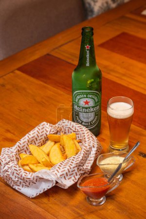 Foto de Papas fritas rústicas, un aperitivo típico brasileño, servido con mayonesa y salsa de chile. Servido con la famosa cerveza Heineken - Imagen libre de derechos