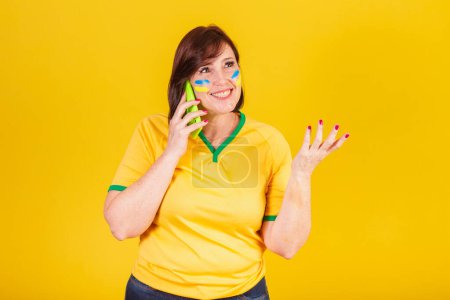 Téléchargez les photos : Femme rousse, fan de football brésilien. appel vocal par téléphone portable, smartphone. - en image libre de droit