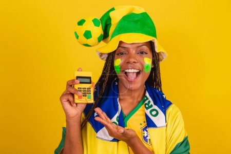 Photo for Black woman young brazilian soccer fan. showing credit card machine. Credit debit. card payment. - Royalty Free Image