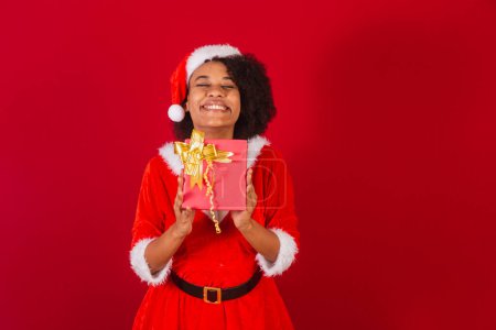 Téléchargez les photos : Belle femme brésilienne noire, habillée en Père Noël claus, maman claus, tenant présent très heureux - en image libre de droit