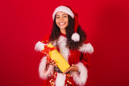 Foto de Hermosa mujer negra brasileña, vestida como santa claus, ropa de Navidad. sosteniendo regalo amarillo. - Imagen libre de derechos