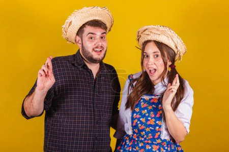Photo for Beautiful couple wearing typical clothes for the Festa Junina. Fingers crossed, twisting, wishing. luck. Prize draw. - Royalty Free Image