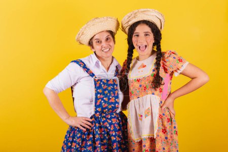 Photo for Grandmother and granddaughter dressed in typical Festa Junina clothes. Hands on hips, smiling. - Royalty Free Image