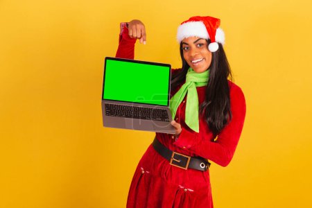 Photo for Beautiful black Brazilian woman, dressed in christmas clothes, santa claus, notebook and showing green chroma screen. - Royalty Free Image