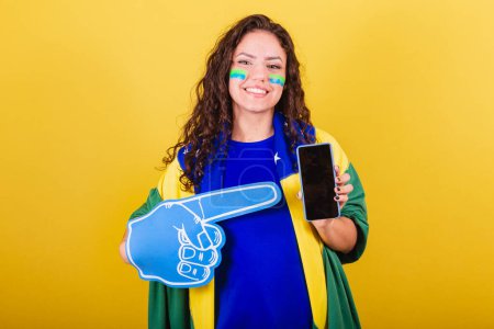 Photo for Woman soccer fan, fan of brazil, world cup, holding cellphone and showing screen. - Royalty Free Image