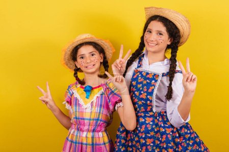 Photo for Sisters and friends, wearing typical clothes of the Festa Junina. Making peace and love sign with fingers. - Royalty Free Image