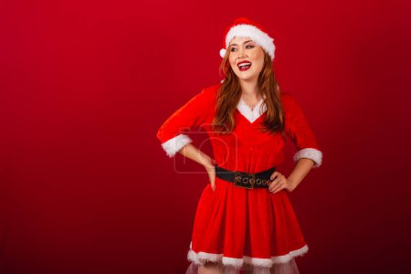 Foto de Hermosa brasileña pelirroja, vestida con ropa de Navidad, Santa Claus. mano en la cintura. - Imagen libre de derechos
