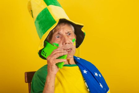 Téléchargez les photos : Femme âgée, fan de football du Brésil, acclamant avec le drapeau. téléphone portable, smartphone - en image libre de droit