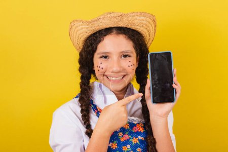 Photo for Girl wearing typical clothes for Festa Junina. pointing to mobile, apps, technology. For the Arraia party - Royalty Free Image