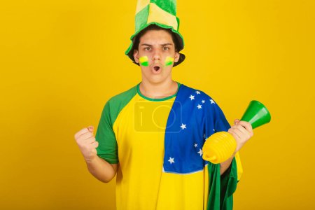 Foto de Joven aficionado al fútbol brasileño. vestido de verde, festejando con bandera brasileña. - Imagen libre de derechos