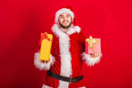 Photo for Caucasian, Brazilian man dressed in Christmas outfit, Santa Claus. holding two gifts. - Royalty Free Image
