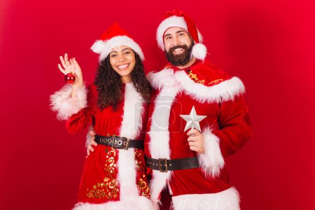 Photo for Brazilian couple, dressed for christmas, santa claus, mummy claus. holding christmas decoration, star, approved, black woman and caucasian man. - Royalty Free Image