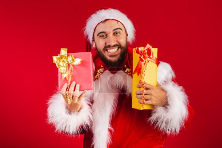 Photo for Brazilian man, dressed in santa claus clothes, giving two presents to camera. - Royalty Free Image