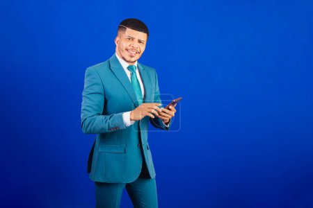 Téléchargez les photos : Homme noir brésilien, vêtu d'un costume et cravate bleue. homme d'affaires. en utilisant votre smartphone - en image libre de droit