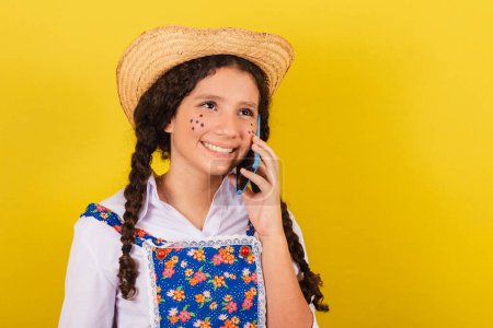 Foto de Chica vestida con ropa típica para Festa Junina. en la llamada de voz por teléfono celular, conectado, llamada, sonriendo. Para la fiesta de Arraia - Imagen libre de derechos