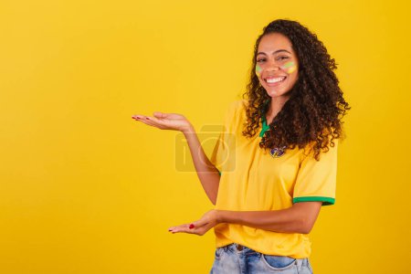 Photo for Young black Brazilian woman, soccer fan. presenting with hands to the left, publicity photo - Royalty Free Image