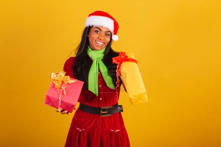 Foto de Hermosa mujer brasileña negra, vestida con ropa de Navidad, Santa Claus, entregando dos regalos. - Imagen libre de derechos