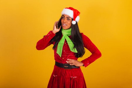 Photo for Beautiful black Brazilian woman dressed in christmas clothes, santa claus, smartphone and voice call - Royalty Free Image