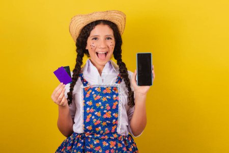 Foto de Chica vestida con ropa típica para Festa Junina. celebración de teléfonos celulares y tarjetas bancarias, aplicaciones, compras móviles. Para la fiesta de Arraia - Imagen libre de derechos