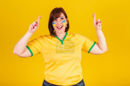 Téléchargez les photos : Femme rousse, fan de football brésilien. signe de chance, doigts croisés, souhait, acclamations. - en image libre de droit
