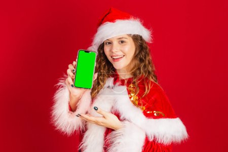 Foto de Mujer brasileña, vestida con traje de Santa Claus, sosteniendo teléfono inteligente con pantalla verde en Chroma. - Imagen libre de derechos