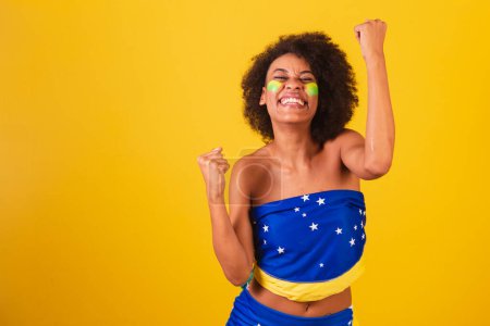 Téléchargez les photos : Jeune femme noire fan de football brésilien. célébrer, vibrer et faire la fête. - en image libre de droit