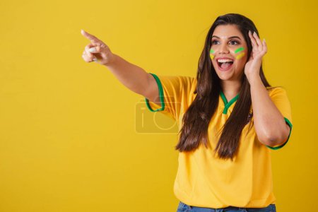 Photo for Woman supporter of Brazil, world cup 2022, football championship, surprised, amazing, pointing away with fingers to the left. - Royalty Free Image