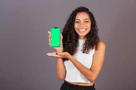 Téléchargez les photos : Jeune femme noire brésilienne tenant un téléphone portable et montrant l'écran, photo publicitaire. - en image libre de droit