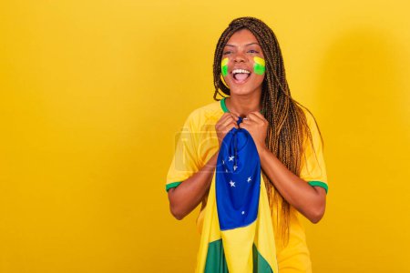 Foto de Mujer negra joven aficionada al fútbol brasileño. sosteniendo la bandera de Brasil, ansioso, viendo el partido. - Imagen libre de derechos