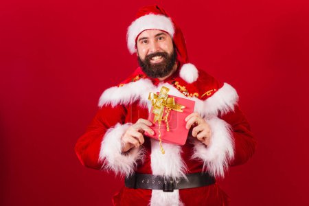 Téléchargez les photos : Santa claus brésilien jeune homme caucasien. tenant cadeau rouge. - en image libre de droit