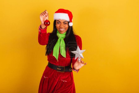 Téléchargez les photos : Belle femme brésilienne noire, vêtue de vêtements de Noël, Père Noël claus, tenant décoration de Noël. étoile et balle. - en image libre de droit