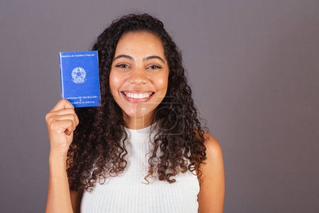 Téléchargez les photos : Jeune femme noire brésilienne tenant portefeuille de travail. CLT, carte de travail et sécurité sociale - en image libre de droit