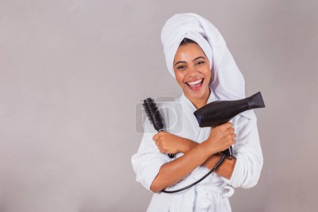 Téléchargez les photos : Belle femme noire brésilienne, portant peignoir et serviette. Tenue sèche-cheveux et brosse, salon de beauté, spa, concept esthétique. - en image libre de droit