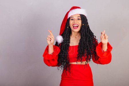 Foto de Mujer negra brasileña vistiendo ropa de navidad, feliz navidad, sonriendo, los dedos cruzados animando, deseando, signo de suerte. - Imagen libre de derechos