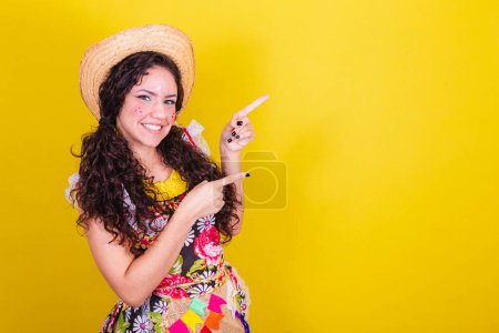 Photo for Beautiful woman dressed in typical clothes for a Festa Junina. Introducing product, space for text and advertisement. - Royalty Free Image