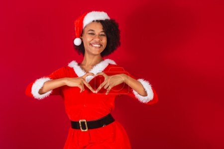 Téléchargez les photos : Belle femme brésilienne noire, habillée en Père Noël claus, maman claus, signe du coeur avec les mains - en image libre de droit