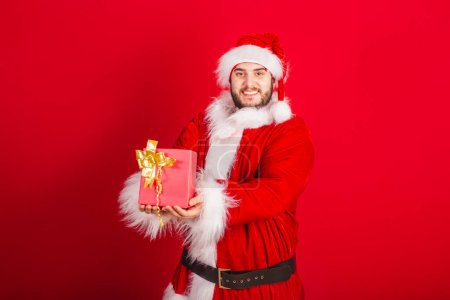 Foto de Caucásico, brasileño vestido con traje de Navidad, Santa Claus. tenencia de regalo rojo. - Imagen libre de derechos