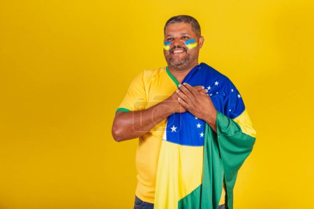Foto de Hombre negro brasileño, fanático del fútbol de Brasil. con la mano en el pecho, gratitud. - Imagen libre de derechos
