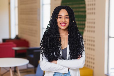 Foto de Joven mujer negra, brasileña, estudiante universitaria en el pasillo de la universidad sonriendo, vestida de blanco. Confiado, optimista. - Imagen libre de derechos