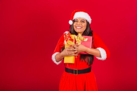 Photo for Beautiful Brazilian woman dressed in Christmas clothes, Santa Claus. hugging two gifts. - Royalty Free Image
