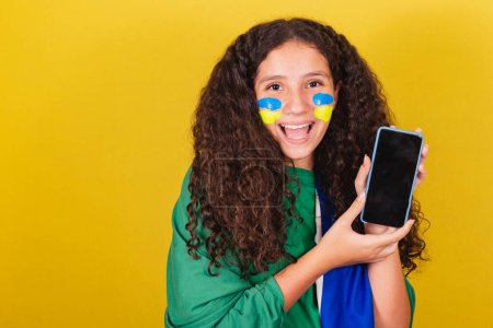 Photo for Brazilian Caucasian girl, soccer fan, holding cellphone, cellphone app, connected world, .World Cup. Olympics. - Royalty Free Image
