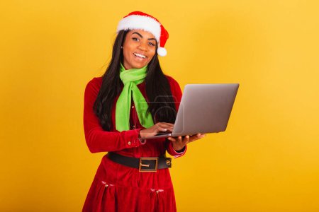 Photo for Beautiful black Brazilian woman, dressed in Christmas clothes, Santa Claus, holding notebook. - Royalty Free Image